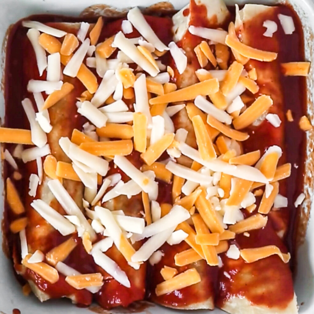 Uncooked enchiladas topped with red sauce and cheese