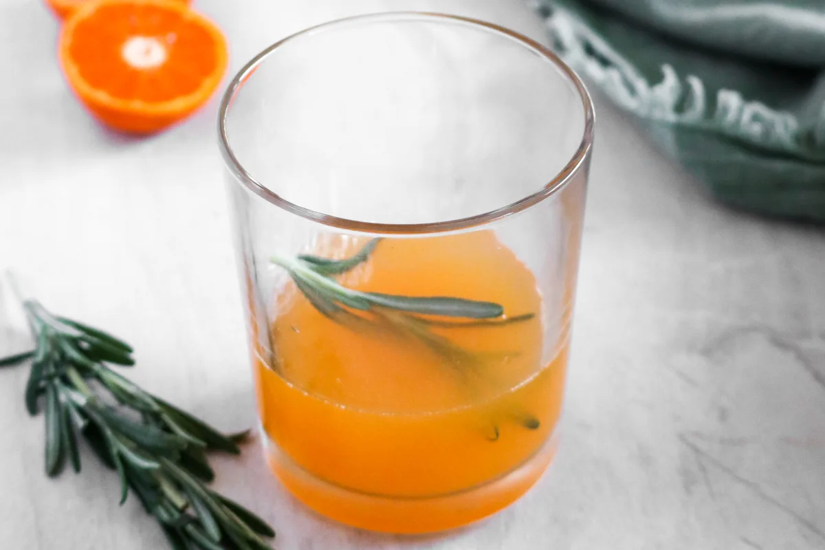 A glass with tangerine juice, lime juice, and rosemary.