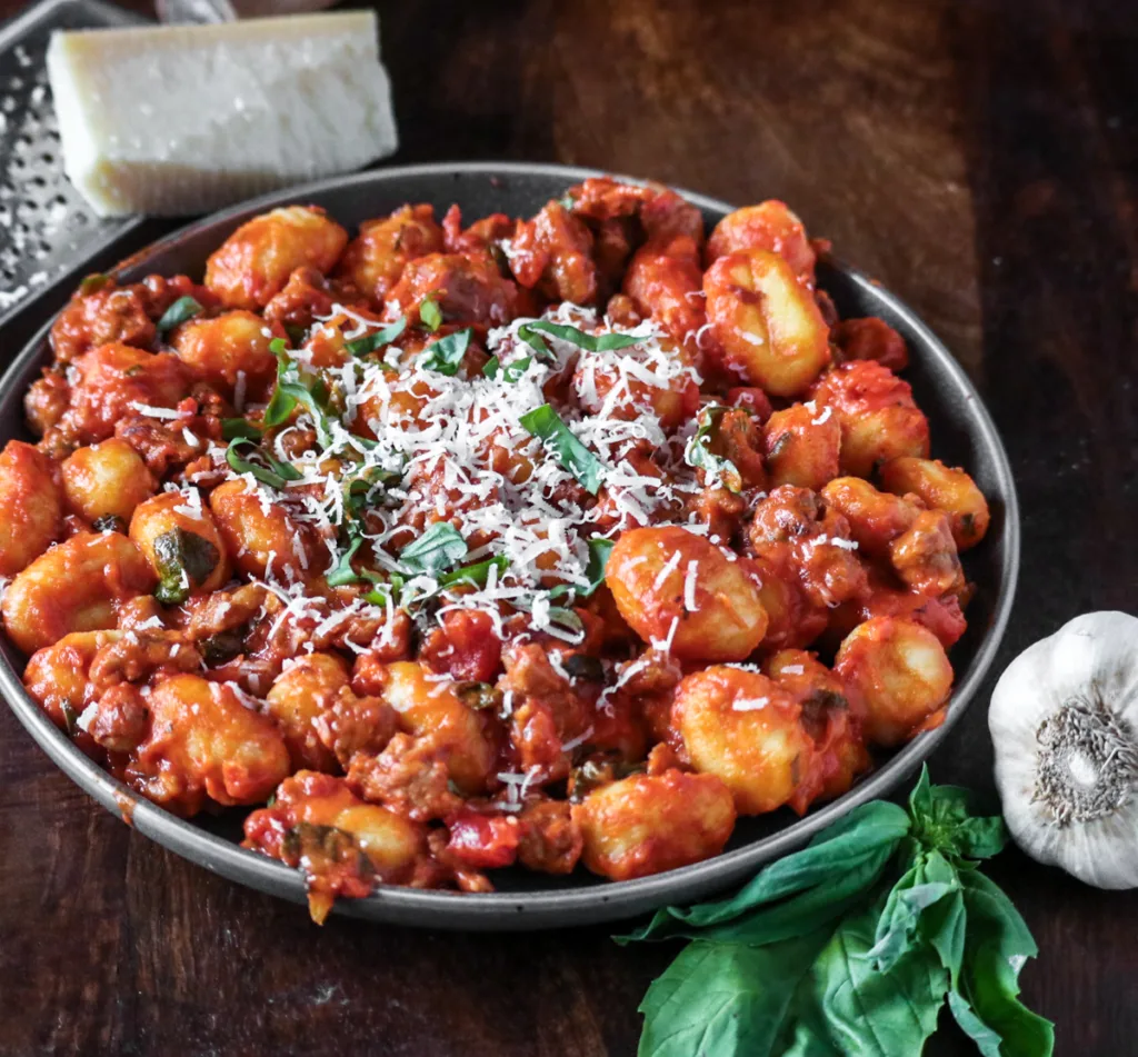 vodka sauce gnocchi with Italian sausage, plated and garnished with freshly grated parmesan and fresh basil.