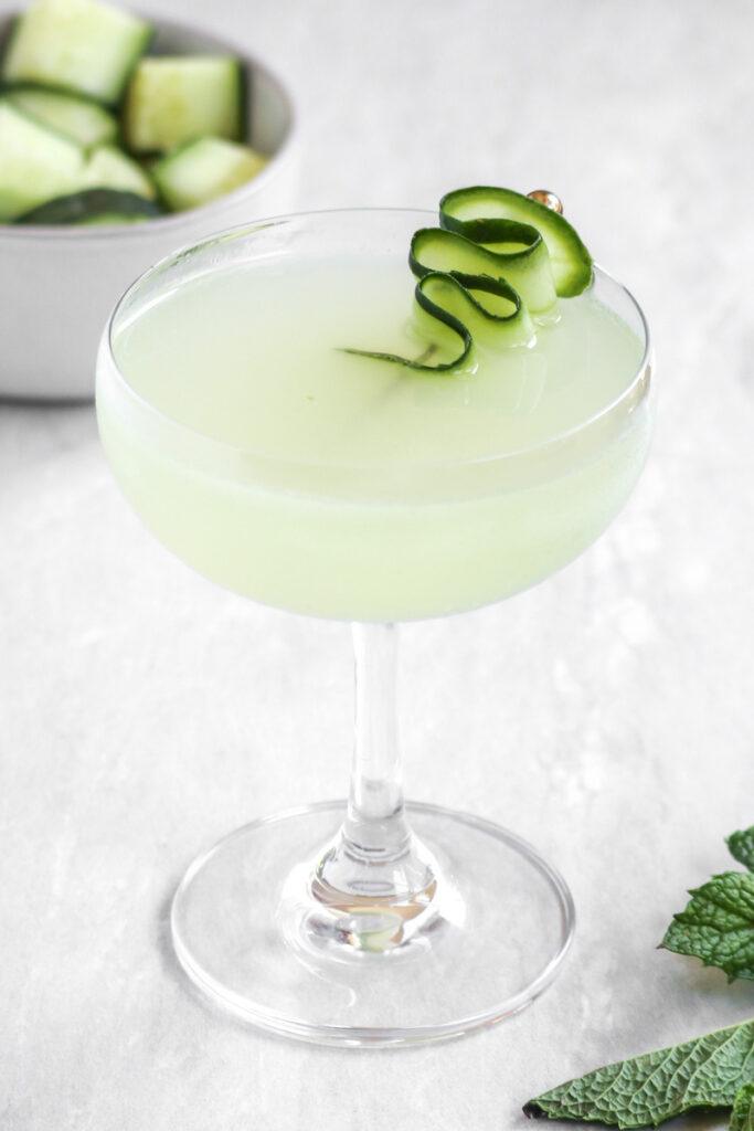 A cucumber mint martini in a coupe martini glass with a cucumber garnish.