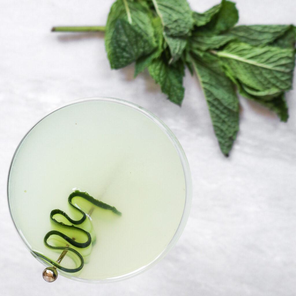 an overhead shot of a cucumber mint martini garnished with cucumber on a white marble countertop