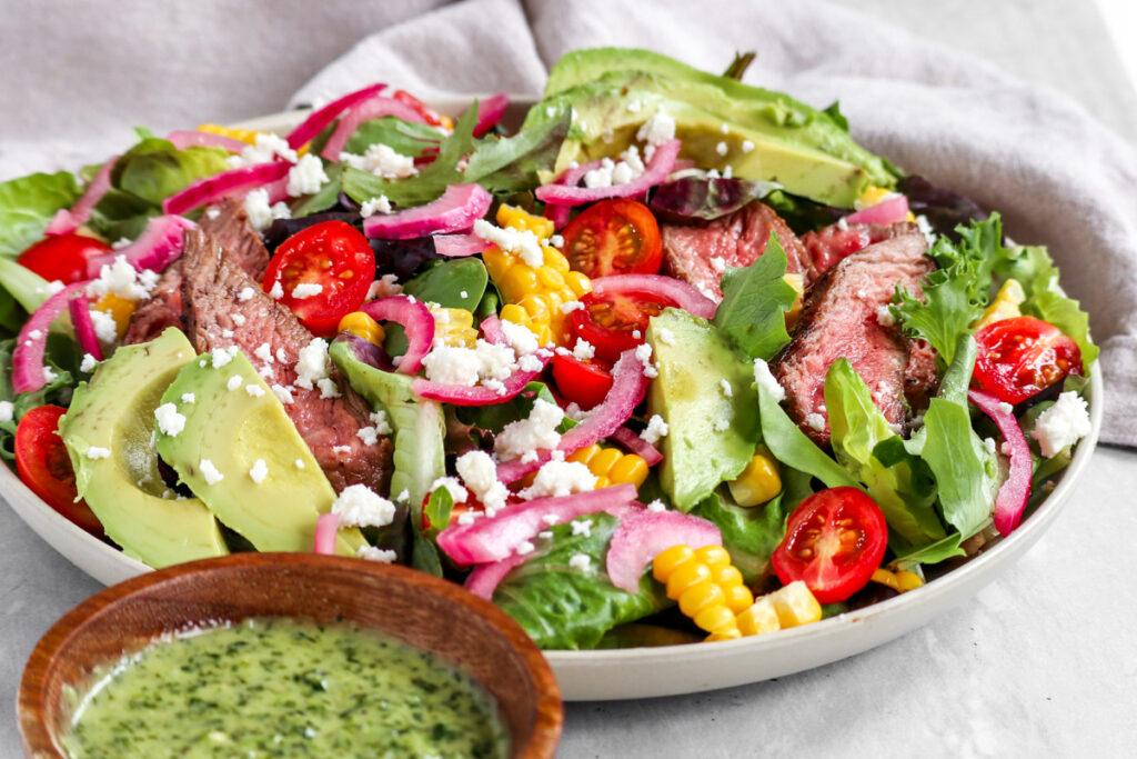 steak salad with tomatoes, corn, tomatoes, avocado and more on a white plate