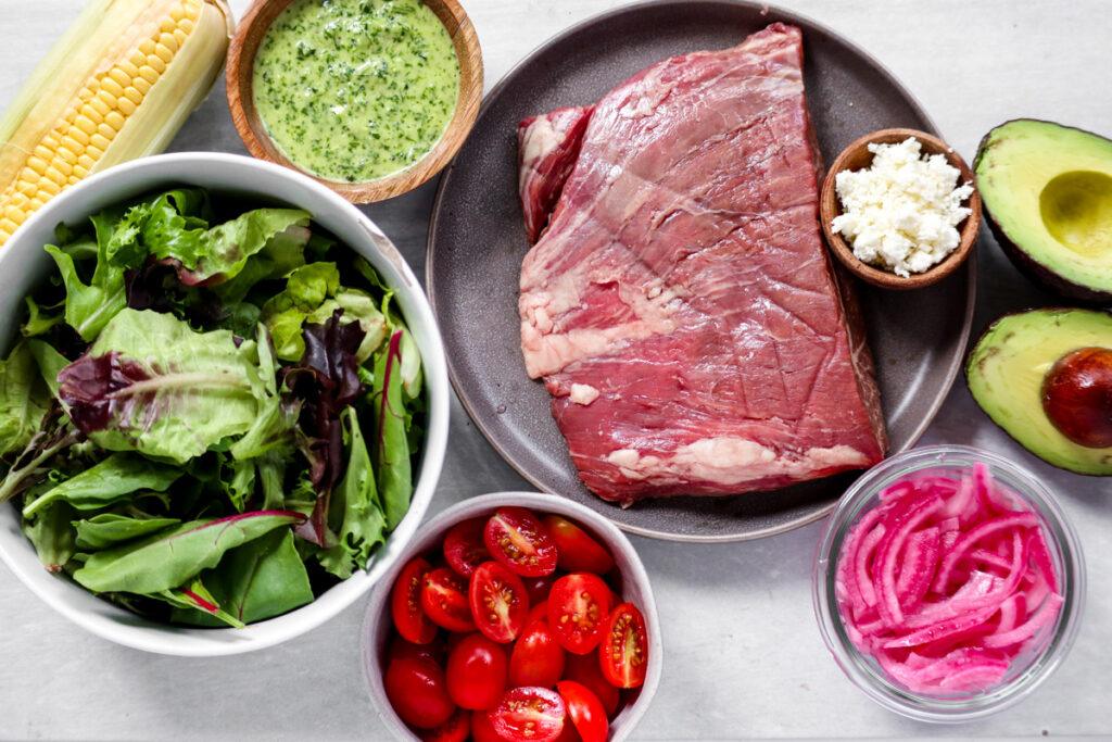 ingredients for the steak salad in separate plates and bowls on white marble